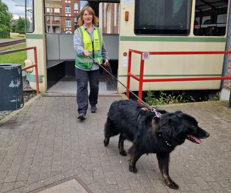 Trainerin Petra von Nasensache - Mantrailing Pur aus Köln geht mit ihrem schwarten Hund aus einem Straßenbahnausgang heraus.